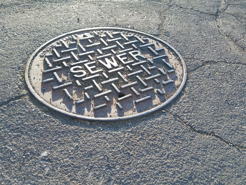 Metal sewer cap on a dry, cracking road during summer